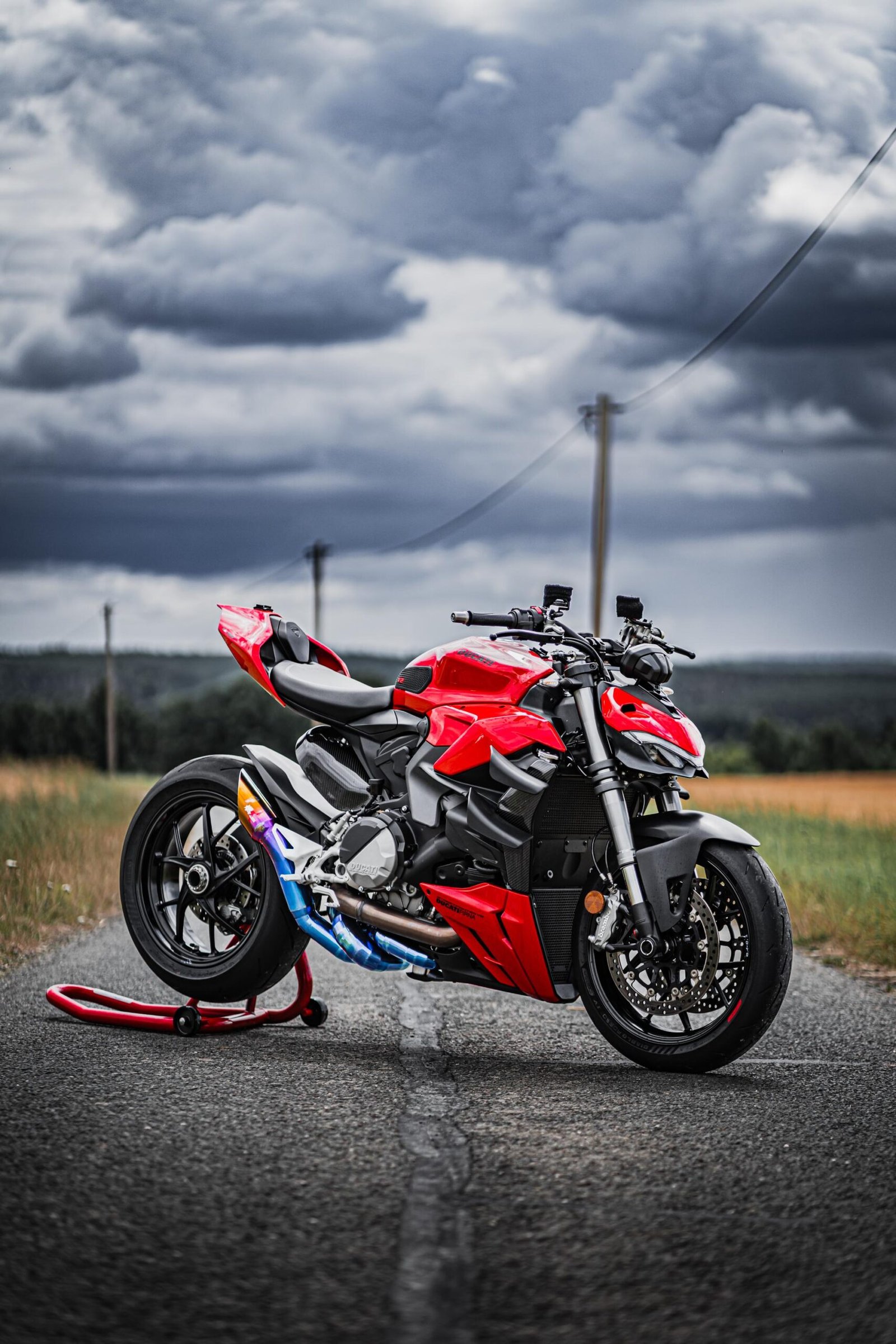 Red sports motorcycle on rural road, cloudy sky.
